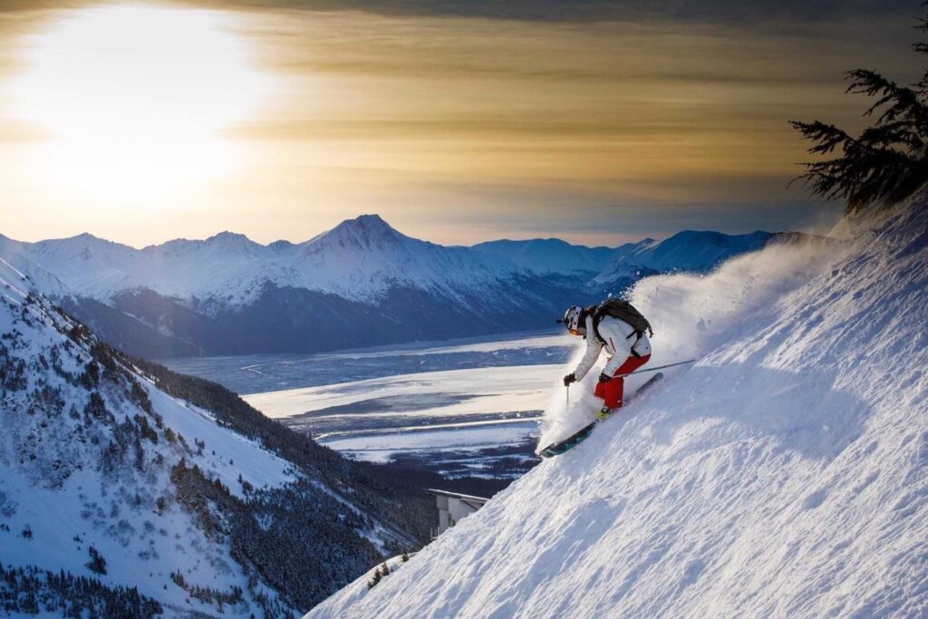 Person skiing down Alyeska Ski resort with snow-covered mountains behind them