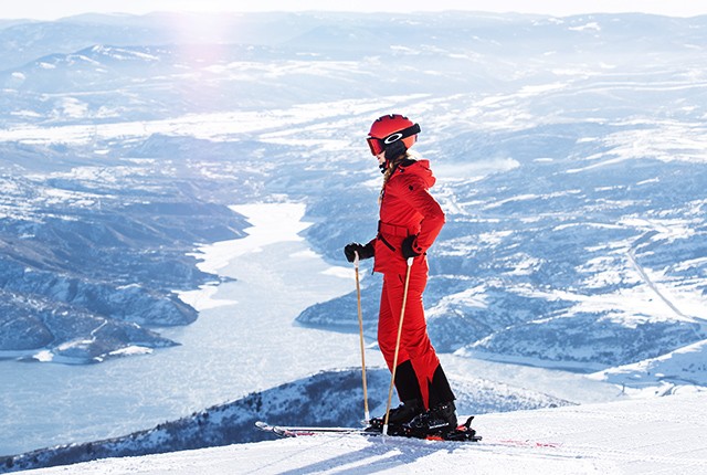 Deer Valley Resort skier standing by lake in red ski outfit.