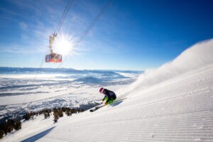 Skier skiing down groomed slope on bluebird day beneath gondola