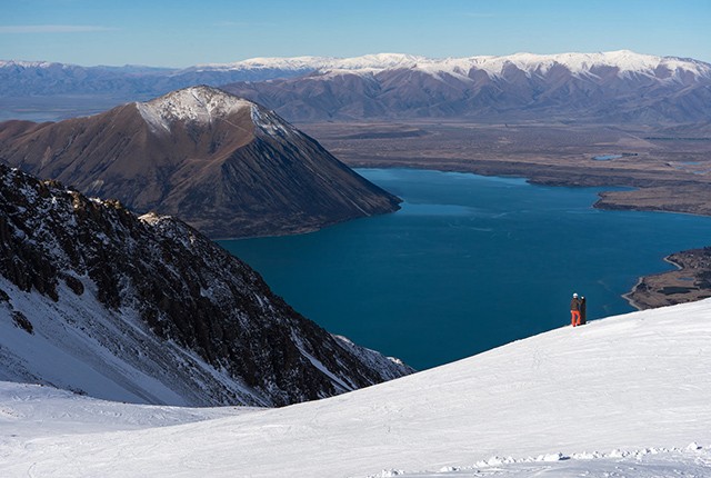 The Remarkables, New Zealand, snowboarder looking out onto expansive view of the mountains and lake.