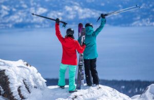 Couple of skiers raising their arms overlooking Lake Tahoe at Palisades Tahoe