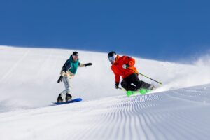 Skier and snowboarder going down groomed slope at Thredbo Resort in Australia on a bluebird day