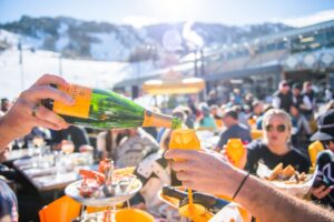 Person pouring champagne in glass with snowy mountains in the background